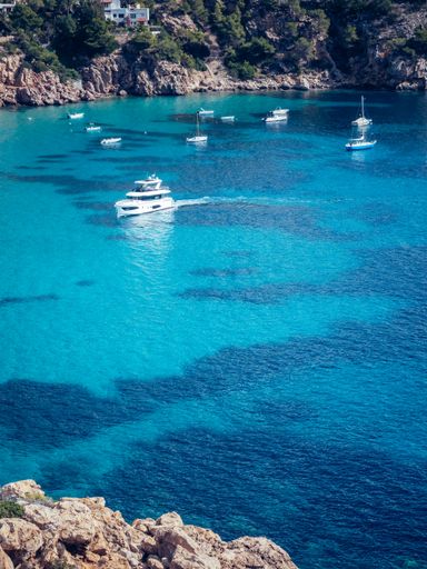A vertical shot of the beautiful crystal azure water of Ibiza island with ships and boats on a sunny day