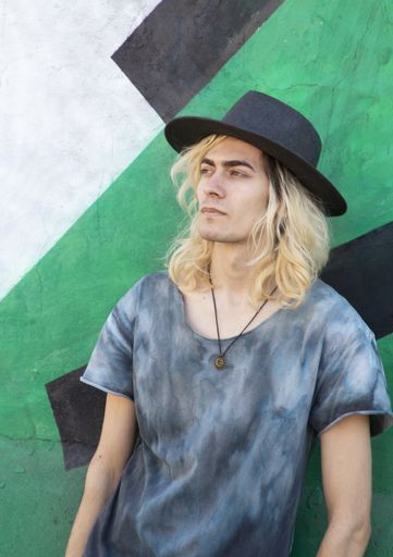 An attractive Armenian guy with a hat leaning on a blue and green wall and looking away