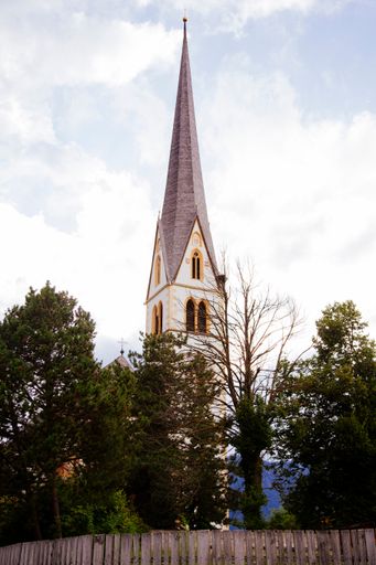 A vertical low angle shot of a tall tower surrounded by lush greenery on a bright summer day