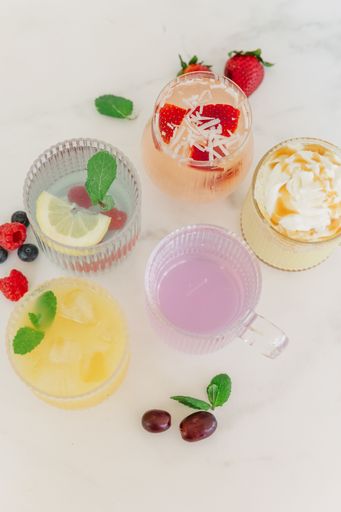 Top view of assorted colorful drinks with fresh fruit and mint on a marble surface.