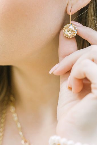 Close-up of a woman's hand holding a gold earring with gemstones, showcasing elegant jewelry design.