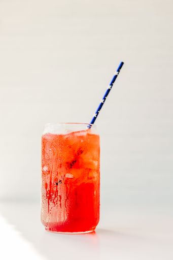 Refreshing red drink with ice cubes in a glass and a striped straw