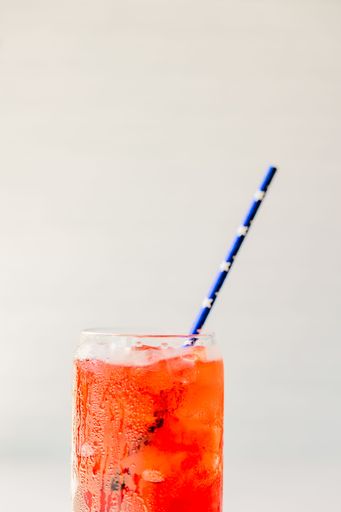Refreshing red drink with ice cubes in a glass and a striped straw