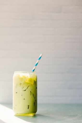 Iced matcha latte in a clear glass on a colorful table with a pastel backdrop.