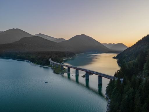 A drone shot of the bridge over Sylvenstein Lake, Bavarian Alps. Mountains covered with dense green woods and blue water of the lake