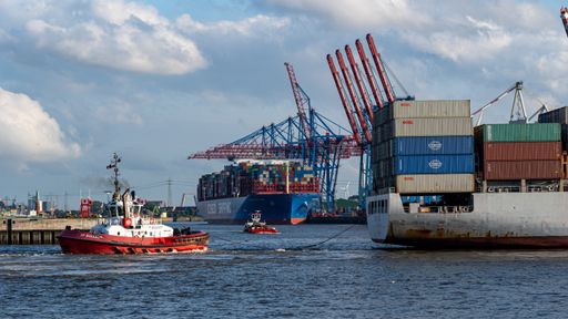 A panoramic shot of the port of Hamburg with a tugboat pushing a container ship out of the harbor