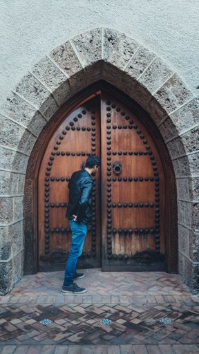 A vertical shot of a male standing in front of a brick wall, opening the wooden door, Castle Palace Counts of Cervellon Anna, Spain