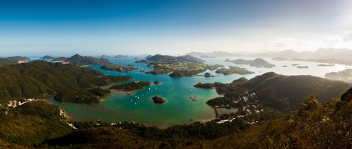 A panoramic shot of forested mountains near the sea under a blue sky