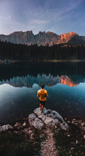 A vertical shot of a person standing near the Lake Carezza surrounded by the Dolomites in South Tyrol, Italy