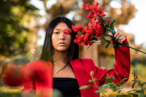 A portrait of an elegant East Asian woman wearing a red suit and posing in a garden in autumn in Spain