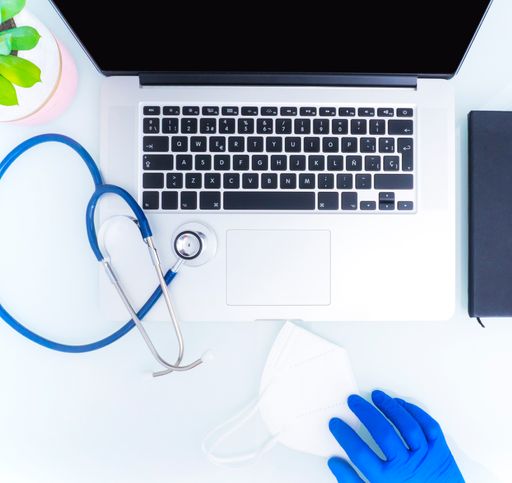 Stethoscope, laptop and notebook on white table. Hand with blue glove holds a mask. Medical concept.