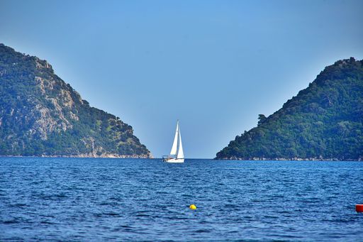 A serene view of a sailboat navigating between lush green hills under a clear blue sky, capturing the essence of peaceful sailing.