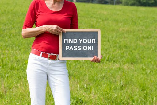 A mid-aged female outdoors in the field holding a blackboard with the text "find your passion!"