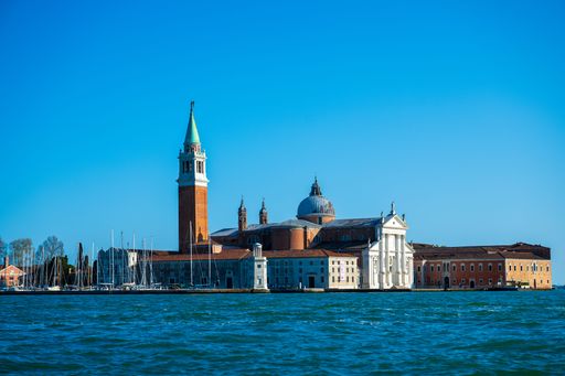 A scenic view of San Giorgio Maggiore island in Venice with clear blue sky and calm water.