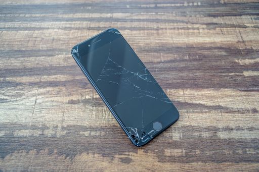 A closeup of the broken glass screen of an iPhone 7 smartphone on a wooden table