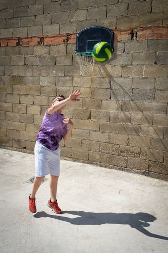 A vertical shot of a young caucasian male playing in the backyard near the basketball hoop