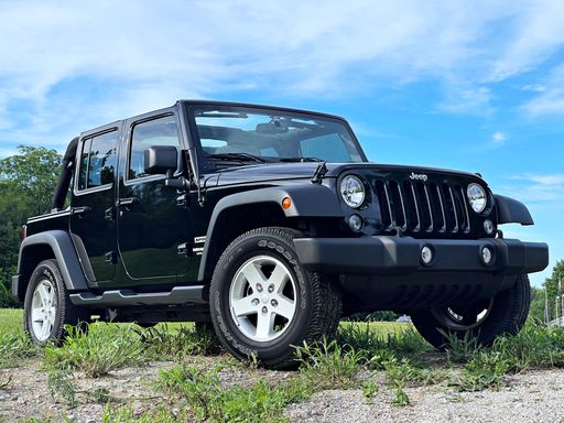 A closeup of a 2015 Black Jeep Wrangler parked on a grassy hill in Waterville, the US