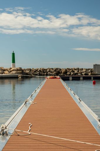 Wooden pier in the sea with a stone wall and a lighthouse in the background on a sunny day