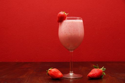 A fruity cocktail served with fresh strawberries on a red wall background