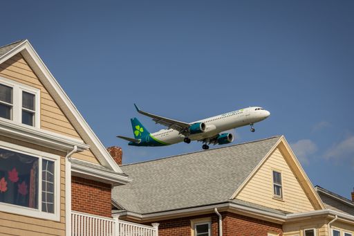 Aer Lingus plane approaches Boston over rooftops, showcasing green and white livery against clear sky