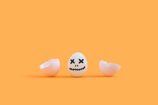 A closeup of a cracked egg painted as a ghost for Halloween isolated on a yellow background
