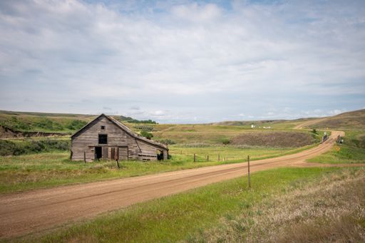 A horizontal shot of a destroyed wooden home on a sunny green field under a cloudy sky on the horizon