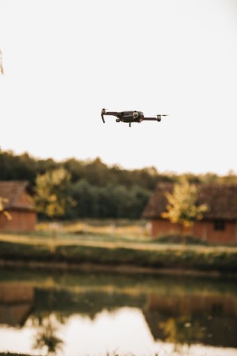 A vertical shot of a small drone with a lake and colorful trees on the background