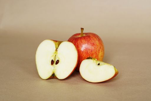 A closeup shot of a red apple with a cute slice on a brown background