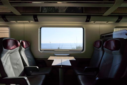 Interior of a modern train with empty seats and a scenic ocean view through the window, showcasing travel comfort and serenity.