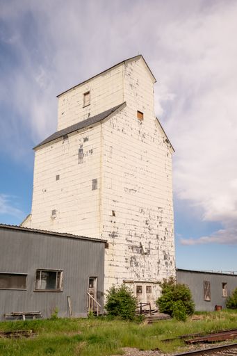 A vertical shot of an old white building of a Grain Elevator against a blue cloudy sky on a sunny day