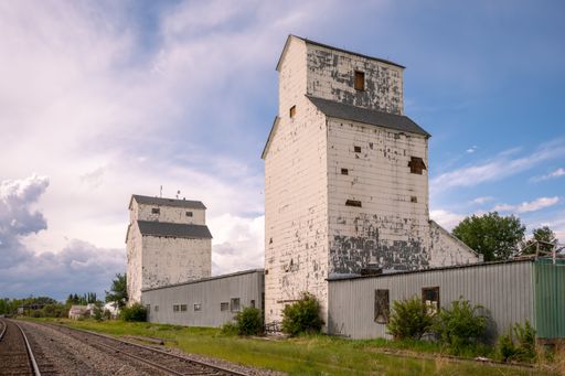 A vertical shot of an old white building of a Grain Elevator against a blue cloudy sky on a sunny day