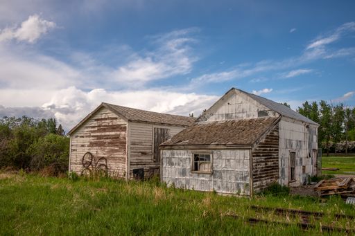 A horizontal shot of two old destroyed wooden home on a sunny green field under a sky on the horizon