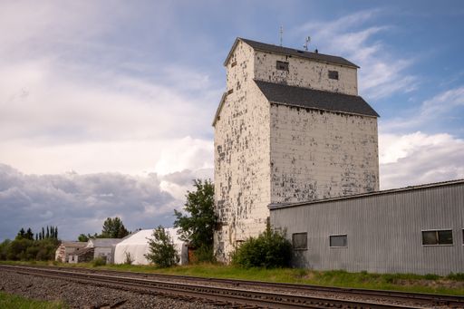 A vertical shot of an old white building of a Grain Elevator against a blue cloudy sky on a sunny day