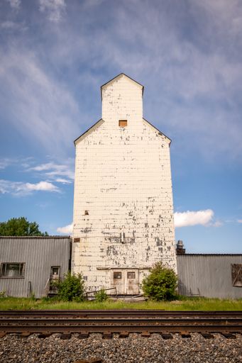 A vertical shot of a white building of a grain elevator  against a blue cloudy sky on a sunny day