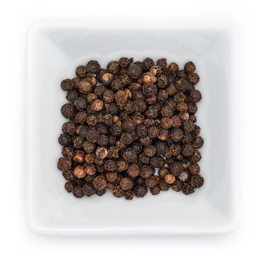 A top view of black peppercorns spice in a white bowl