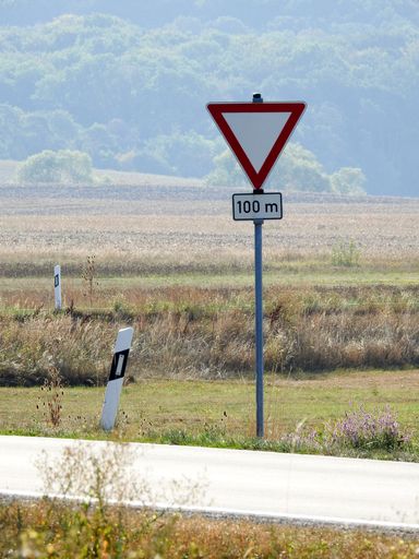 A vertical shot of a roadside warning sign of "give way in 100 meters"