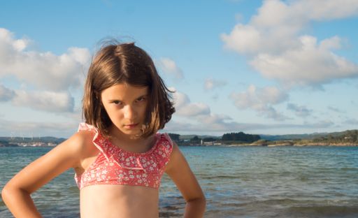 The picture shows a portrait of a Caucasian girl with angry gesture on the beach