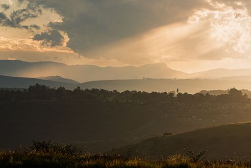 A scenic view of rolling hills under a dramatic sky with sun rays breaking through clouds, creating a serene and atmospheric landscape.