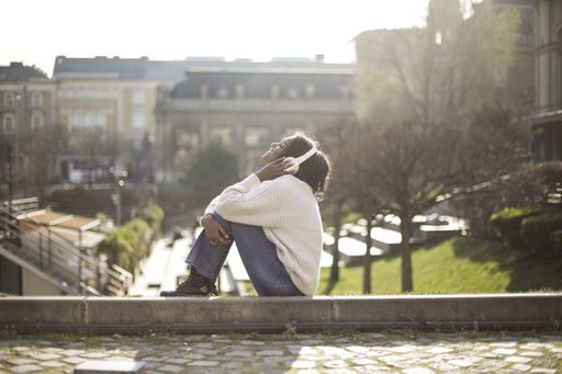 A side shot of a young student sitting in the park and listening to music in headphones
