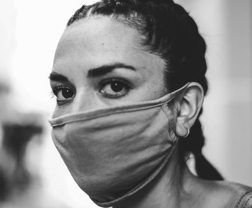 Black and white portrait shows a woman wearing a face mask, with only their eyes and the upper part of their face visible.