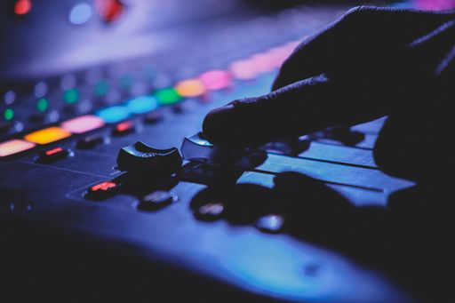 Close-up of a hand adjusting a sound mixer with colorful lights in a dimly lit studio environment.
