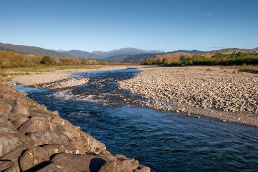 Scenic view of a flowing river with rocky banks and distant mountains under a clear blue sky, capturing the serene beauty of nature.