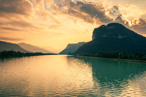 A beautiful view of a flowing river surrounded by green mountains gleaming under the sunset