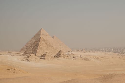 The Pyramids of Giza under a hazy sky, showcasing ancient Egyptian architecture in a desert landscape.