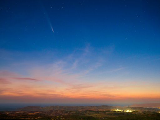 A breathtaking view of a comet streaking across a starry night sky over a serene landscape at dusk.