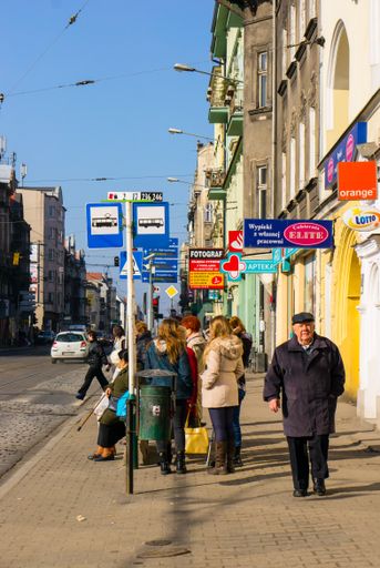 A group of people waiting by a bus stop near small shops in the city Poznan, Poland