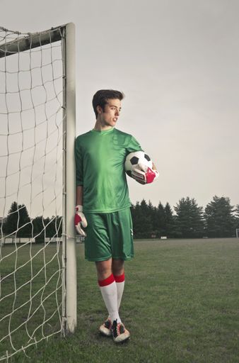 A handsome soccer player in the football field near the gate with a ball in his hands