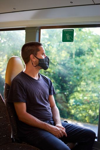A vertical shot of a Hispanic guy wearing a mask and looking out of a bus window