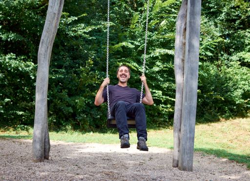 A Hispanic man sitting on a swing in a park