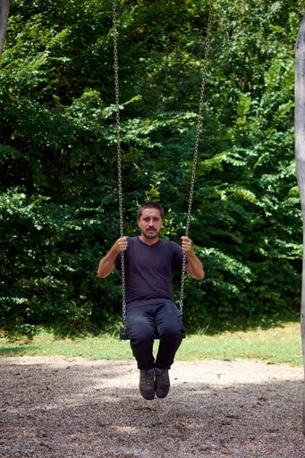 A vertical shot of a Hispanic guy sitting on a swing in a park